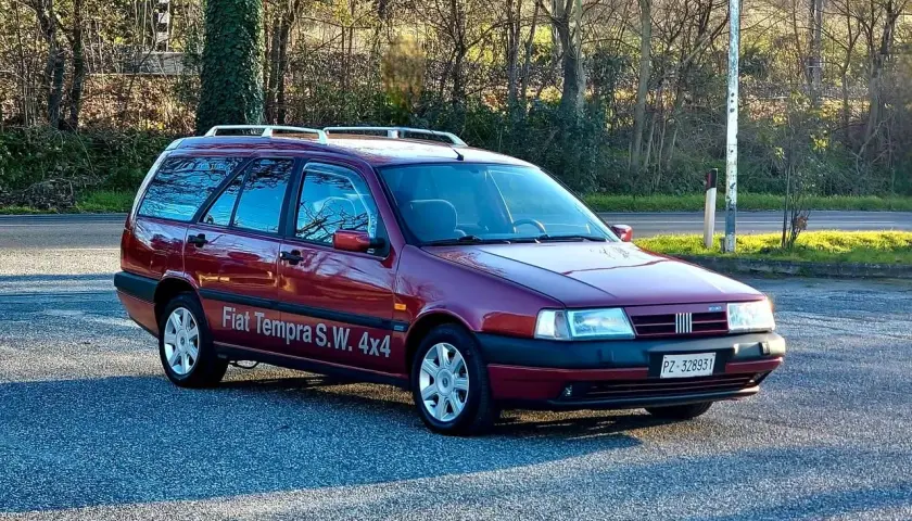 Ciemnoczerwony Fiat Tempra S.W. 4x4 z relingami dachowymi zaparkowany na tle drzew.