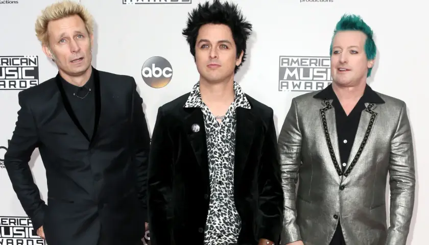 Trzech członków Green Day: Billie Joe Armstrong, Mike Dirnt i Tré Cool, pozują na czerwonym dywanie.