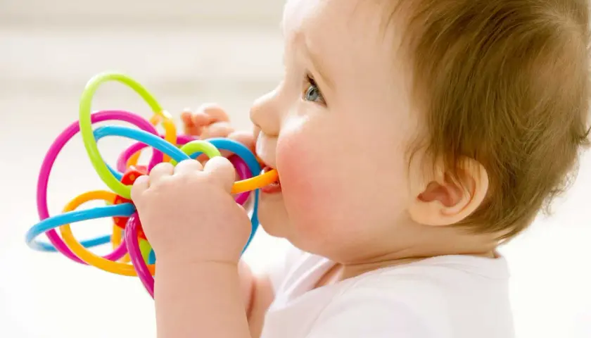 Bambino di 1 anno con dolore ai denti, che morde un giocattolo colorato per alleviare il fastidio.