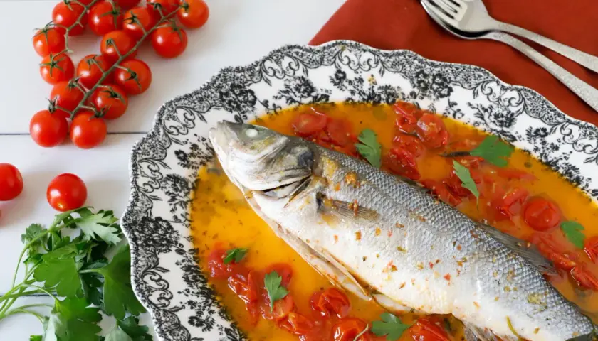 Spigola all'acqua pazza, un piatto succulento con pomodorini e prezzemolo, pronto per essere gustato.