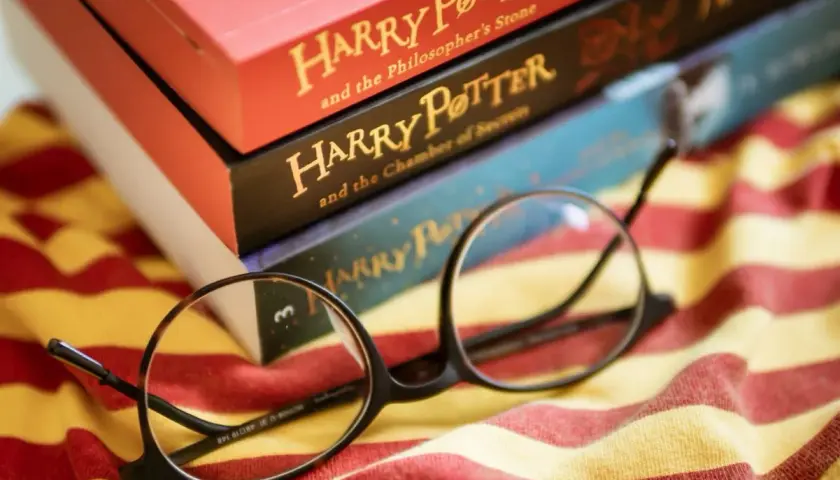 Okulary Harry'ego Pottera leżą na tle książek z serii i szalika Gryffindoru. To idealny cytat z Harrego Pottera dla każdego fana.