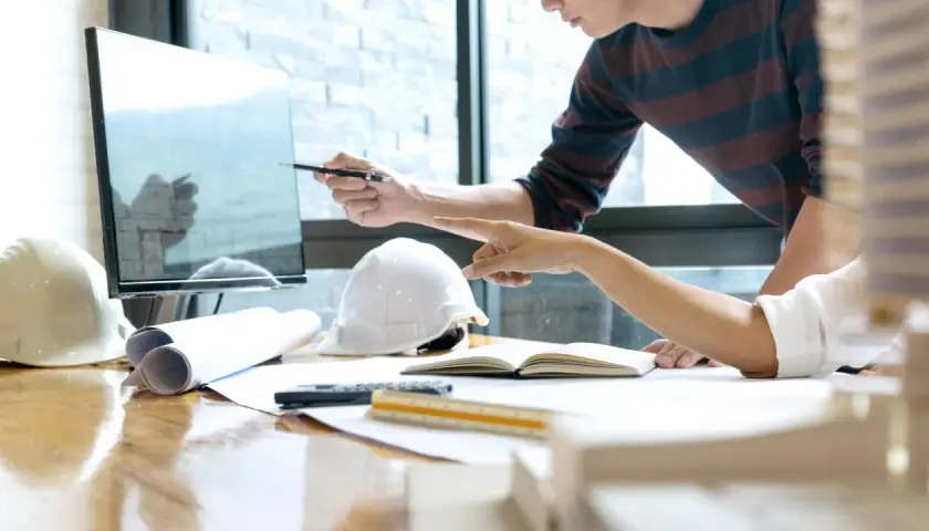 Deux architectes discutent d'un plan sur un écran, utilisant un système de gestion de contenu d'entreprise pour organiser leurs documents.