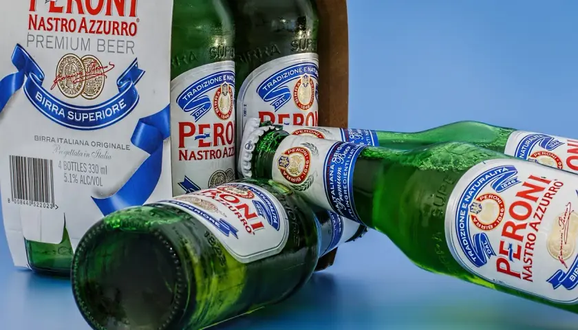 Butelki piwa Peroni Nastro Azzurro leżą obok kartonu. W jakiej temperaturze zamarza piwo? Poniżej 0°C, ale lepiej pić je schłodzone.