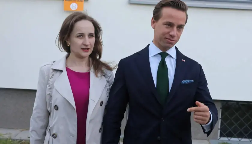 Kobieta w różowej sukience i jasnym płaszczu obok mężczyzny w granatowym garniturze.