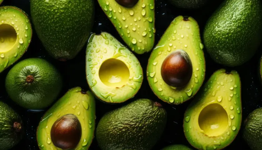 Aguacates frescos y jugosos, cortados y enteros, con gotas de agua, resaltando sus increíbles propiedades nutritivas.