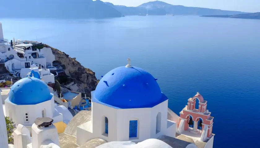 Białe domy i niebieskie kopuły kościołów na Santorini, idealne miejsce na wakacje. Dowiedz się, jak dolecieć na Santorini.
