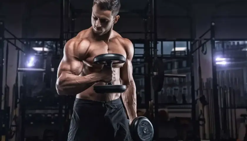 Mężczyzna ćwiczy biceps z hantlami. Ile serii na biceps w tygodniu? To pytanie zadaje sobie wielu trenujących.