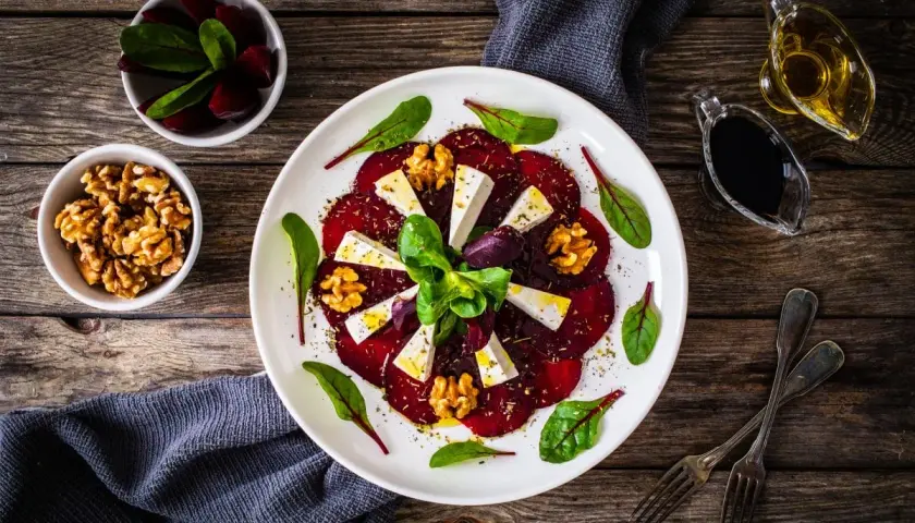 Eleganckie carpaccio z buraka z serem feta, orzechami włoskimi i świeżymi ziołami, podane na białym talerzu.