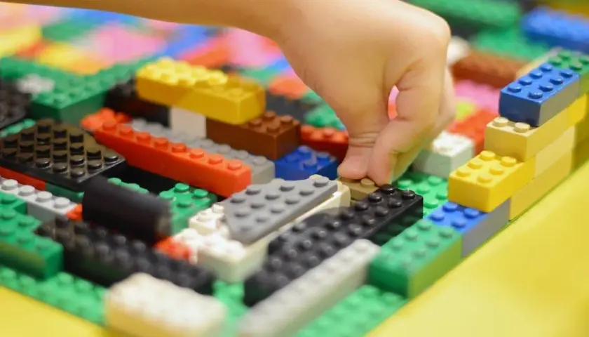 Kind baut mit bunten LEGO-Steinen. Viele LEGO-Ideen zum Nachbauen sind hier zu sehen, von einer Hand, die einen Stein platziert.