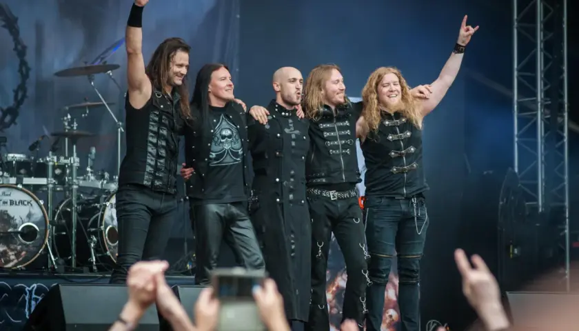 Zespół Beast in Black na koncercie, pięciu muzyków w czarnych strojach pozuje na scenie.