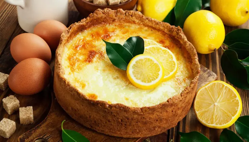 Un délicieux flan au citron, garni de rondelles de citron et de feuilles vertes, entouré de citrons frais, d'œufs et de sucre.
