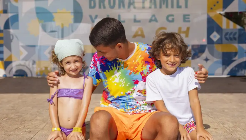 Un uomo con due bambini sorridono davanti a uno sfondo con la scritta "Brora Family Village".