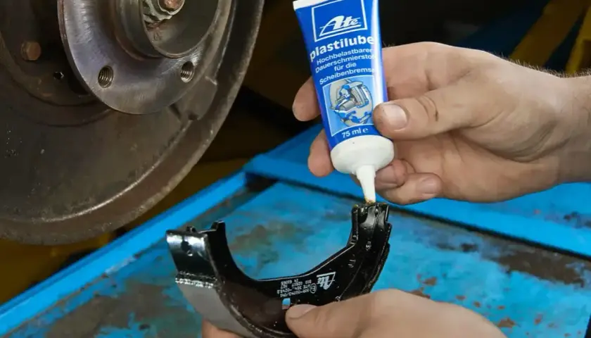 Mechanik aplikuje smar ceramiczny do hamulców na szczękę hamulcową, przygotowując ją do montażu.