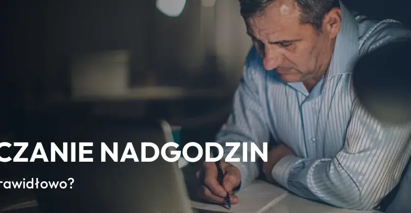 Mężczyzna pracuje po godzinach, rozliczając nadgodziny. Na ekranie laptopa widać napis "Rozliczanie nadgodzin".