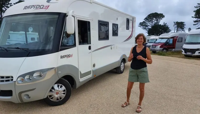 Une femme pose devant son camping-car Rapido, sur une aire de camping-car près de la Côte de Granit Rose.