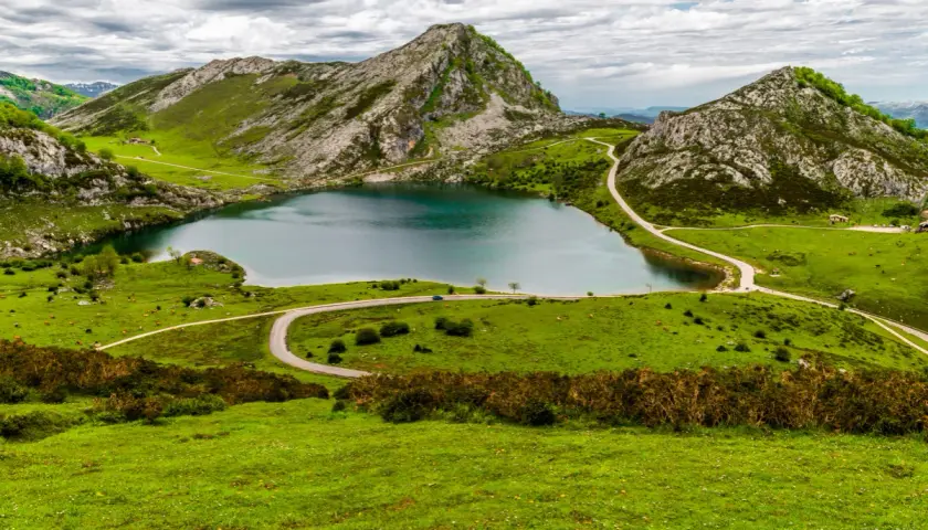 Lago en Picos de Europa que ver: paisaje verde con montañas rocosas, un lago azul y carreteras sinuosas.