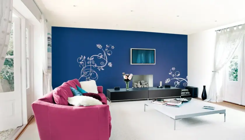 Un salone moderno con divano fucsia e parete blu con decorazioni floreali. Idee per come pitturare un salone con stile.