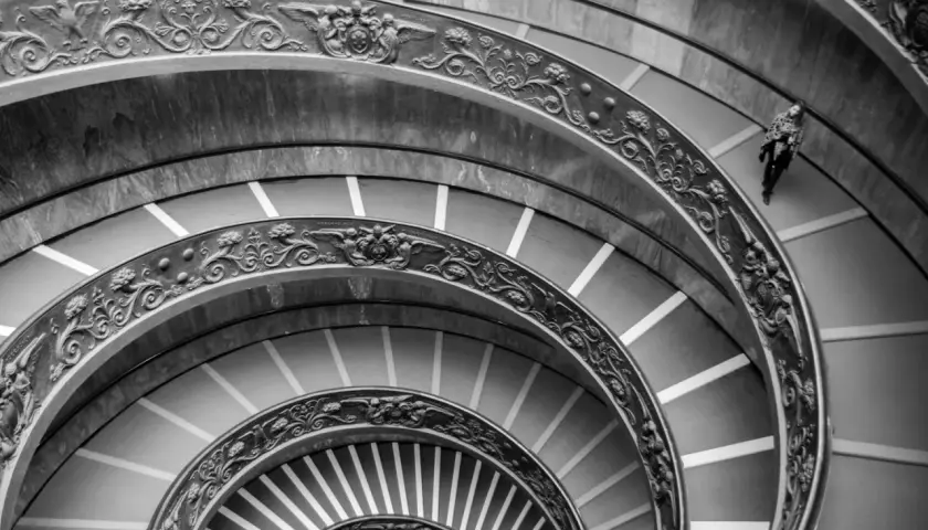 Un escalier en colimaçon orné, rappelant une coupole du Vatican, avec une personne solitaire descendant ses marches.