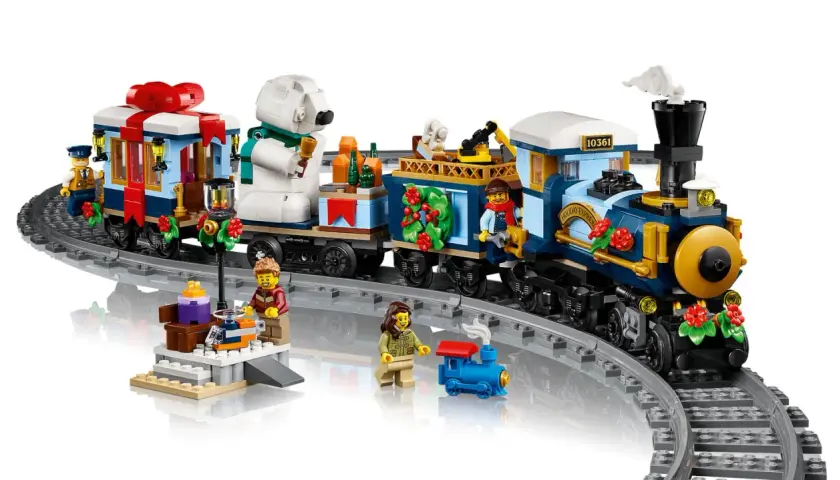 Der LEGO Weihnachtsexpress fährt mit Geschenken und einem Eisbären durch die Winterlandschaft. Figuren warten am Bahnsteig.