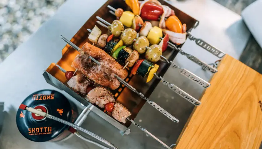 Leckere Spieße mit Lachs, Hähnchen und Gemüse warten auf das Grillen mit Gasgrill. Daneben eine Gasflasche.