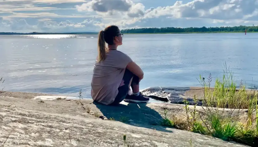 Kvinna sitter på en klippa vid havet, njuter av lugnet. Perfekt för mental avslappning och att ladda batterierna för att sova gott.
