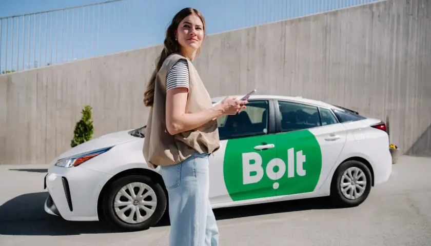 Kobieta z telefonem stoi obok białego samochodu Bolt z zielonym logo.