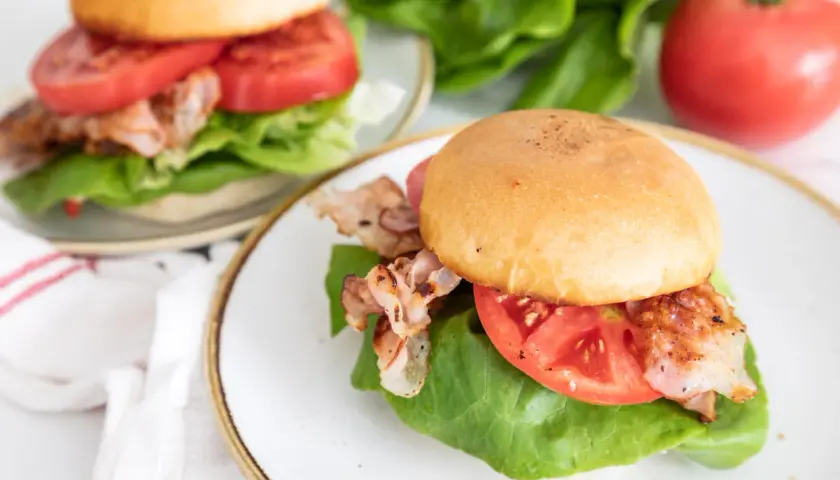 Dwa pyszne BLT na talerzach, z chrupiącym bekonem, soczystymi pomidorami i świeżą sałatą. Idealne na szybki lunch.