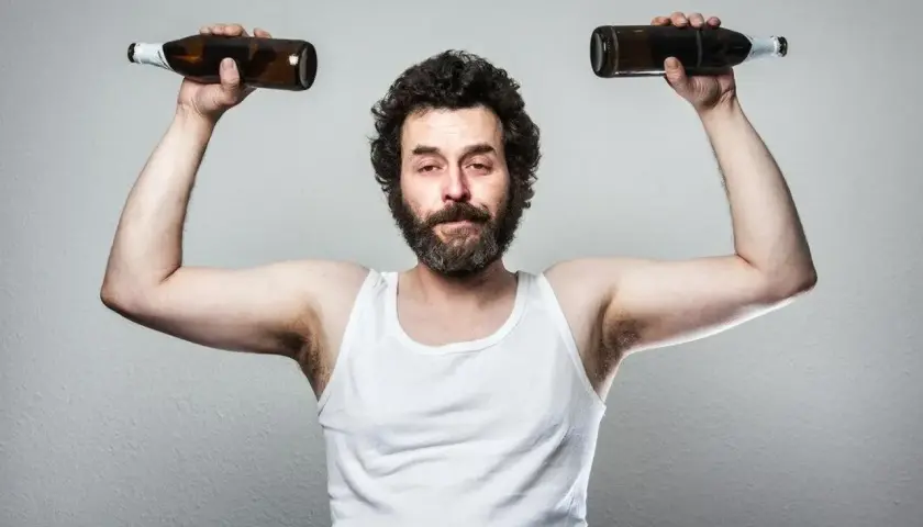Mężczyzna w białej podkoszulce podnosi dwie butelki, symbolizując wpływ testosteronu a alkoholu na siłę i samopoczucie.