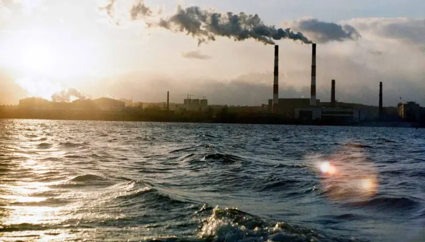 Chimeneas industriales emiten humo sobre un río, un ejemplo de cómo se mide la calidad del aire.