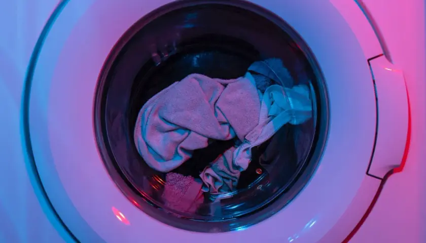 Ein Wäschekorb voller Kleidung, darunter auch AirPods, wartet auf die Waschmaschine.