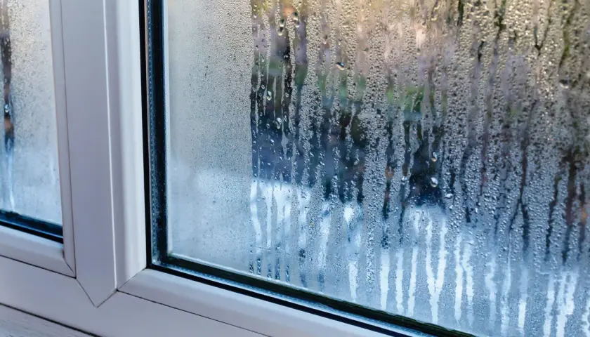 Gouttes d'eau ruisselant sur une fenêtre, signe de condensation. La lumière du jour filtre à travers les gouttelettes.
