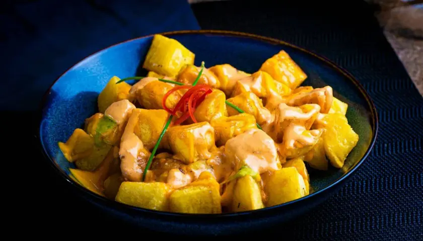 Patatas bravas receta: trozos dorados de patata cubiertos con una cremosa salsa rosada y decorados con pimiento rojo y cebolleta.