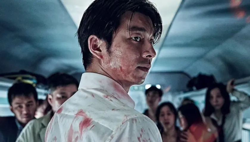 Mężczyzna z zakrwawioną koszulą i twarzą, w tle przerażeni ludzie. Scena z filmów o zombie.