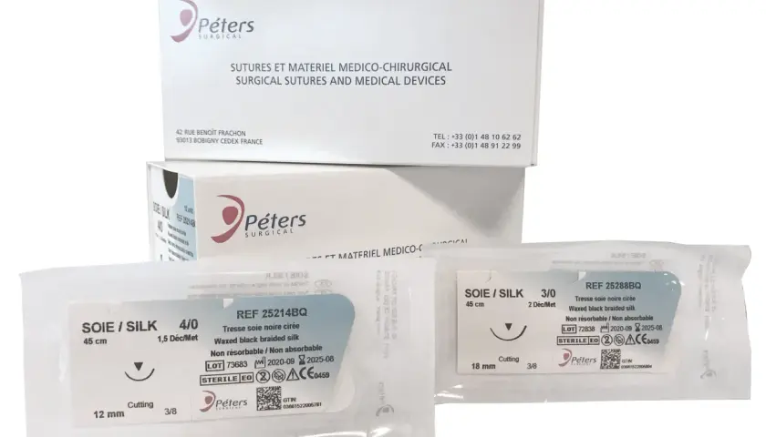 Opakowania z szwami chirurgicznymi Peters Surgical. Widać dwa pakiety z szwami jedwabnymi, w tym jeden z igłą tnącą.
