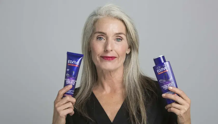 Mujer con cabello gris muestra productos Elvive Color-Vive, ideales como remedios caseros para quitar el amarillo del pelo y matizar.