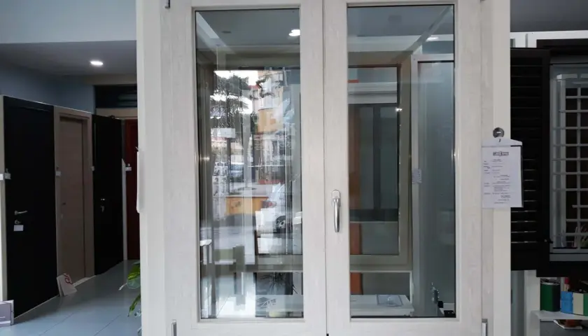Finestra con telaio in alluminio effetto legno, con doppio vetro e maniglia argentata. Sullo sfondo, porte e altre finestre.