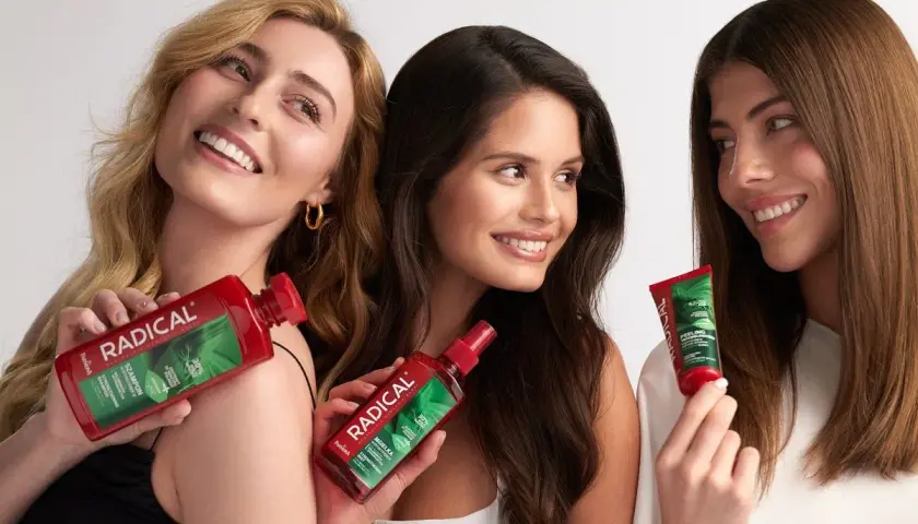 Trzy uśmiechnięte kobiety prezentują produkty Radical: szampon, mgiełkę i peeling. Ich włosy lśnią dzięki tej **radical**nej pielęgnacji.