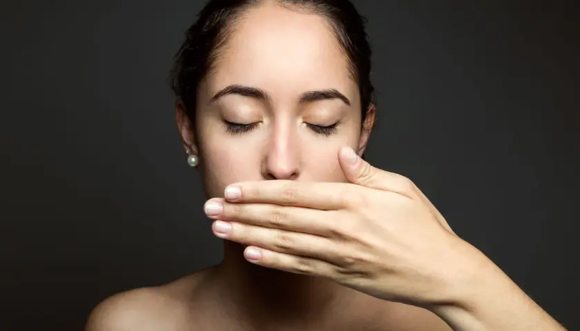 Donna con mano sulla bocca, occhi chiusi, come se avesse scoperto che il filo interdentale puzza.