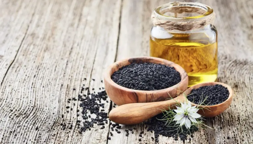 Semi neri in ciotole di legno e un flacone di olio di nigella, con un fiore bianco.