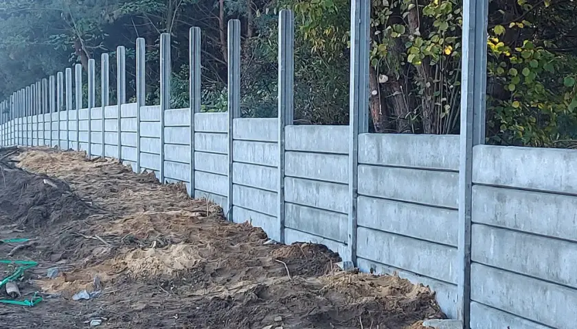 Nowe betonowe słupki ogrodzeniowe czekają na zalanie. Solidna konstrukcja wzdłuż leśnej ścieżki.