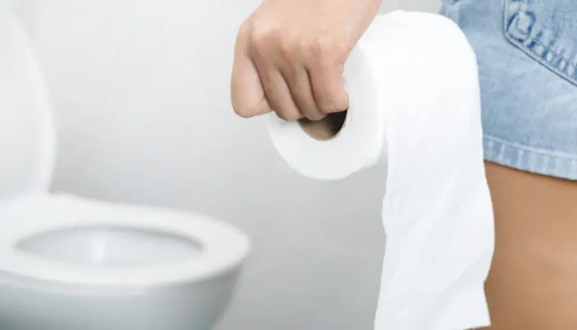 Dłoń trzymająca rolkę papieru toaletowego, w tle sedes. Stres wywołuje biegunka.