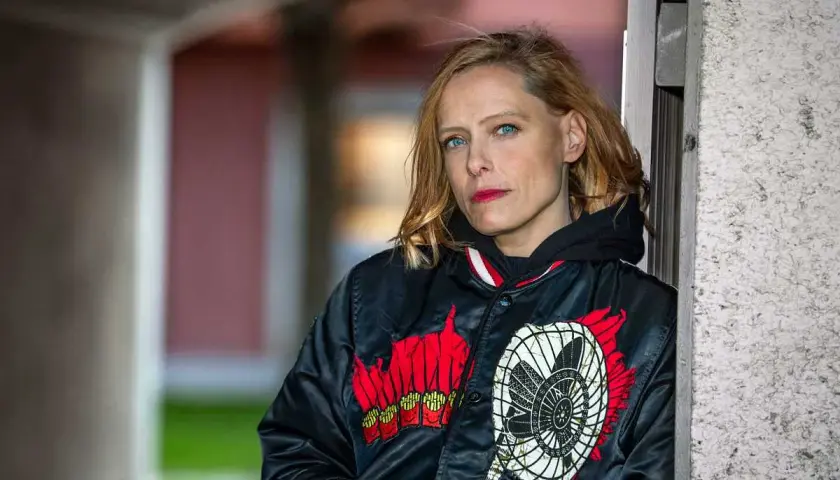 Wanda Bendjelloul, med blå ögon och rött läppstift, bär en svart jacka med en fläkt-design.