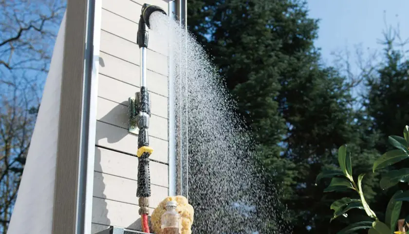 Eine Gartendusche, die man selber bauen kann, sprüht erfrischendes Wasser. Ein Schwamm und eine kleine Flasche stehen bereit.