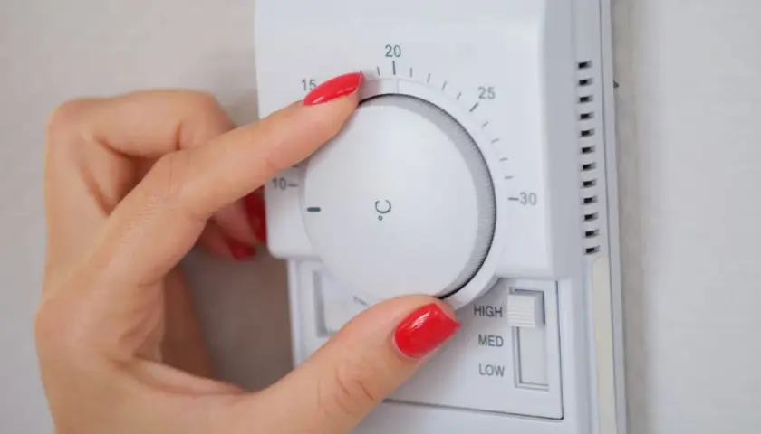 Mano ajustando el termostato para la temperatura calefacción noche. Se ve el dial con grados y el selector de potencia.