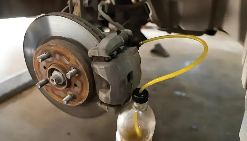 Bleeding car brakes with the cap off the bleed screw, using a yellow tube to drain fluid into a bottle.