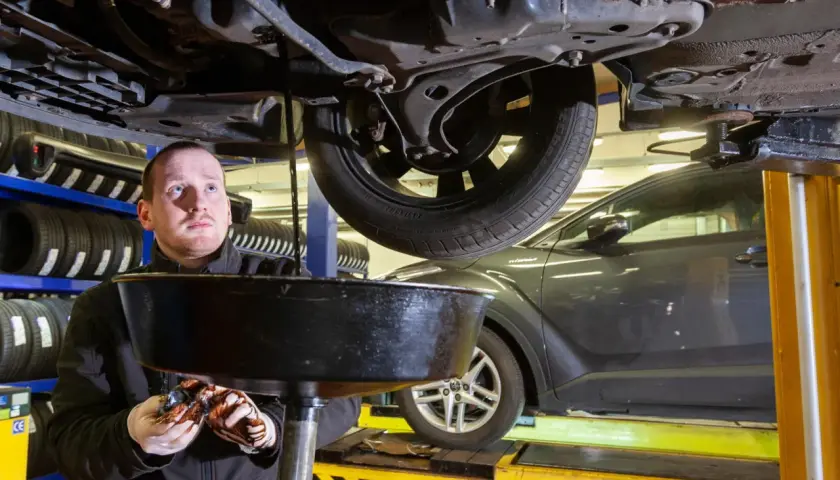 Mechanik spuszcza zużyty olej z samochodu. Dowiedz się, ile kosztuje wymiana oleju w warsztacie.