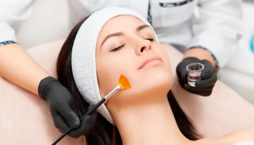 Una esteticista aplica un tratamiento de peeling facial con brocha a una mujer.