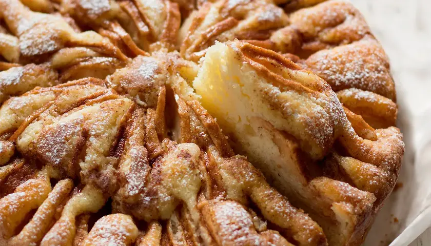 Una deliziosa torta di mele, cosparsa di zucchero a velo, con una fetta sollevata che mostra la morbida consistenza.