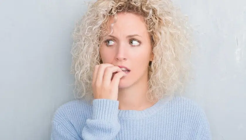 Ragazza con capelli ricci biondi, maglione azzurro, morde le unghie, con brividi di freddo e ansia.