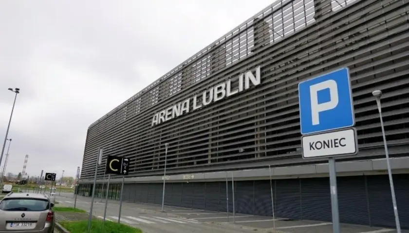 Nowoczesny stadion Arena Lublin z napisem na fasadzie. Obok znak parkingu i drogowskazy.
